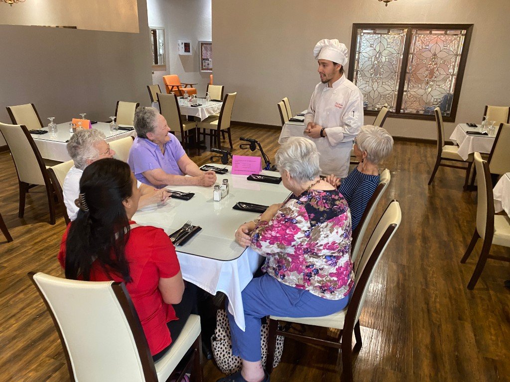 Chef speaking with residents seated around a dining table in the community dining room